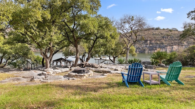 surrounding community with a water view, an outdoor fire pit, and a lawn