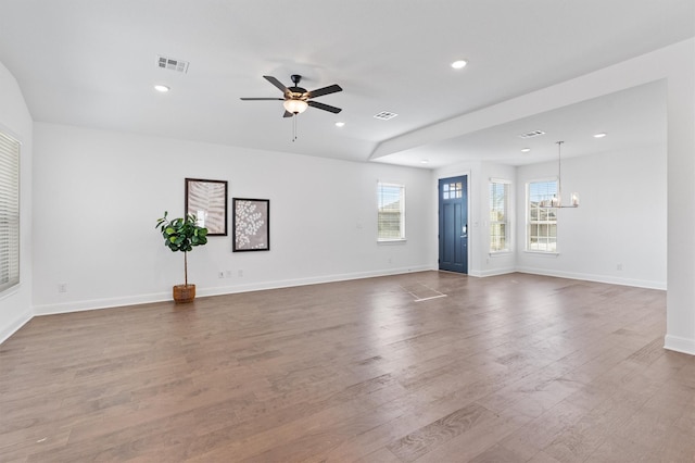 unfurnished living room featuring ceiling fan with notable chandelier and wood-type flooring