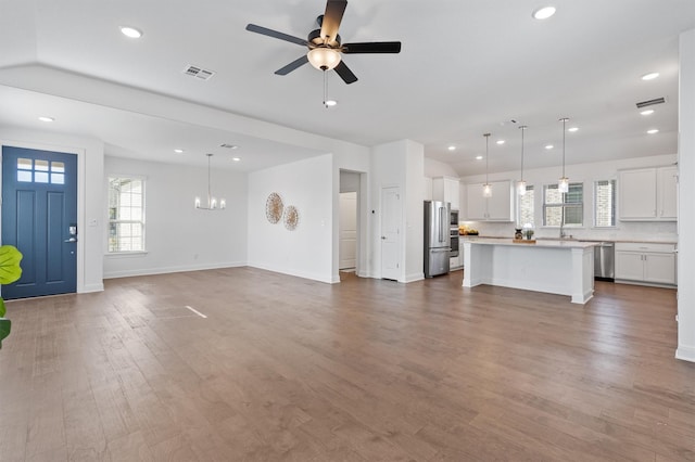 unfurnished living room with a wealth of natural light, ceiling fan with notable chandelier, and hardwood / wood-style flooring