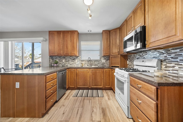 kitchen with tasteful backsplash, kitchen peninsula, sink, light hardwood / wood-style flooring, and appliances with stainless steel finishes