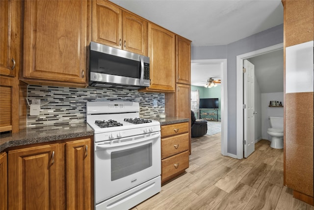 kitchen featuring dark stone counters, backsplash, white gas stove, ceiling fan, and light hardwood / wood-style flooring