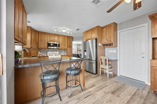 kitchen with tasteful backsplash, a breakfast bar, sink, light wood-type flooring, and stainless steel appliances