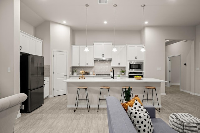 kitchen with pendant lighting, white cabinets, a towering ceiling, stainless steel appliances, and an island with sink