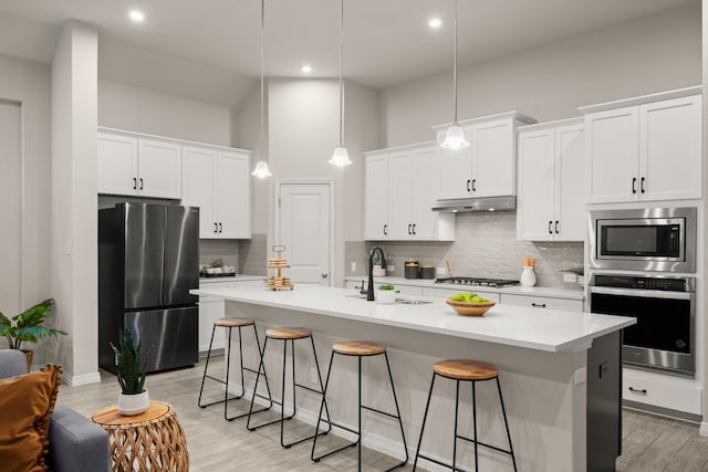 kitchen with appliances with stainless steel finishes, an island with sink, white cabinetry, and pendant lighting