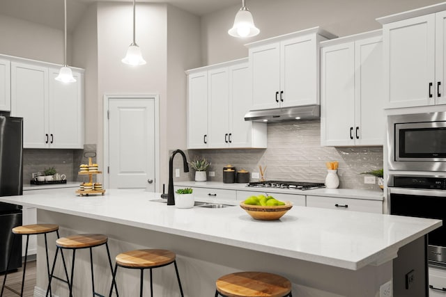 kitchen with hanging light fixtures, appliances with stainless steel finishes, and a kitchen island with sink