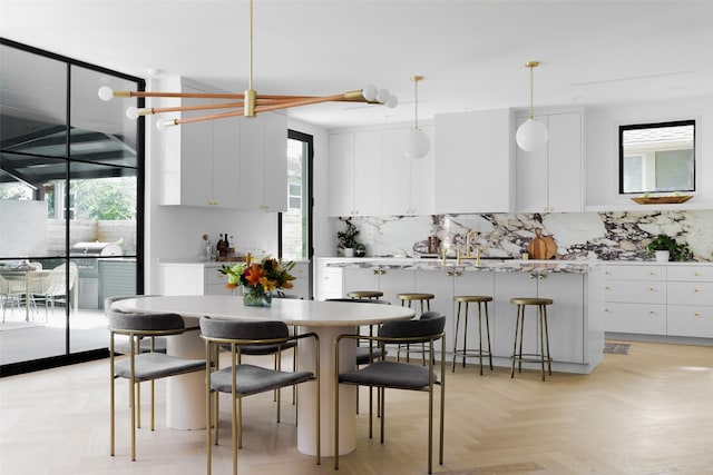 kitchen featuring decorative light fixtures, decorative backsplash, light parquet floors, white cabinetry, and an island with sink