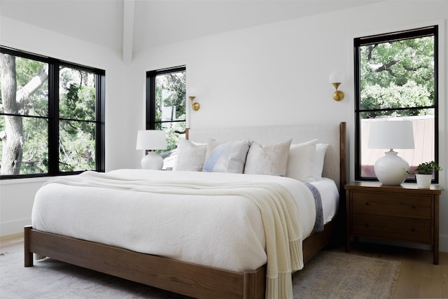 bedroom with wood-type flooring, multiple windows, and beamed ceiling