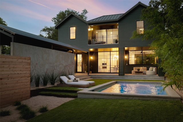 back house at dusk with an outdoor hangout area, a lawn, and a balcony