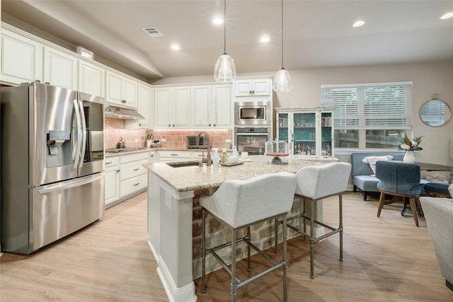 kitchen featuring an island with sink, appliances with stainless steel finishes, hanging light fixtures, light stone countertops, and white cabinets