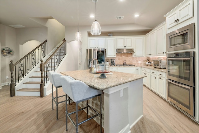 kitchen with light stone countertops, white cabinets, a kitchen island with sink, and stainless steel appliances