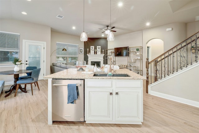 kitchen featuring white cabinetry, a center island with sink, light stone countertops, stainless steel dishwasher, and sink