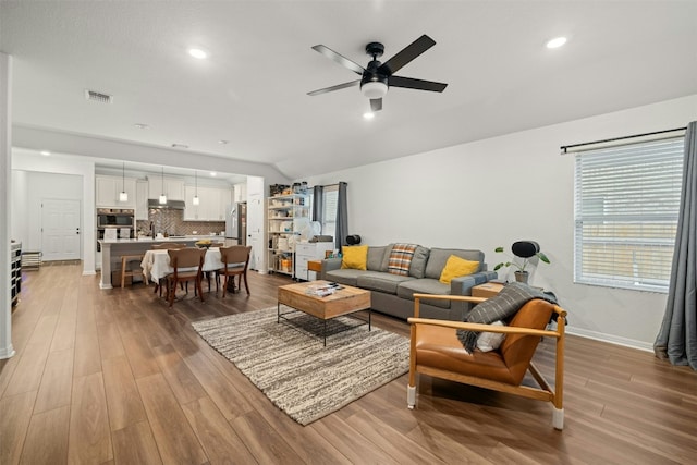 living area featuring visible vents, ceiling fan, light wood-type flooring, and lofted ceiling