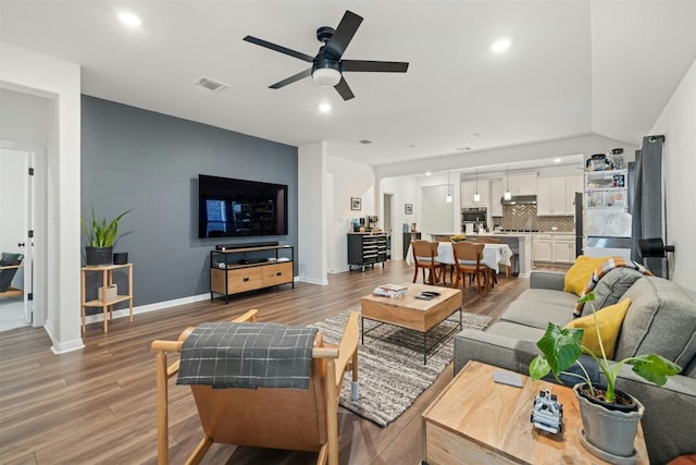 living room featuring a ceiling fan, visible vents, light wood finished floors, baseboards, and recessed lighting