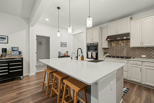 kitchen with stainless steel gas cooktop, dark wood-style flooring, under cabinet range hood, dobule oven black, and backsplash