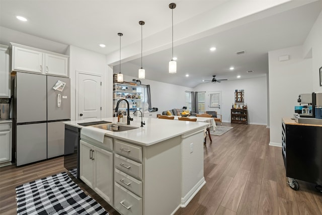 kitchen featuring ceiling fan, decorative light fixtures, sink, stainless steel refrigerator, and an island with sink