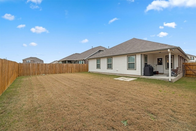 back of house featuring a lawn, roof with shingles, a fenced backyard, and a patio area