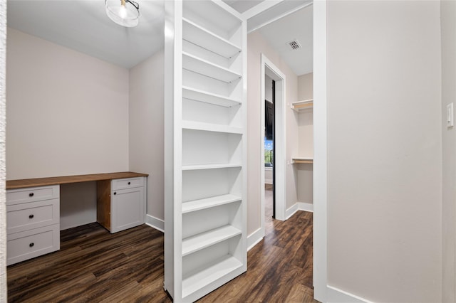 spacious closet featuring dark hardwood / wood-style floors and built in desk