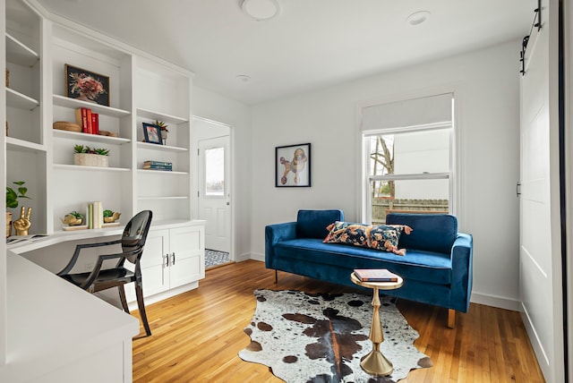 office space featuring built in desk, a barn door, and light wood-type flooring