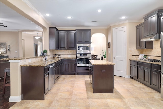 kitchen featuring kitchen peninsula, a breakfast bar area, stainless steel appliances, light stone countertops, and sink