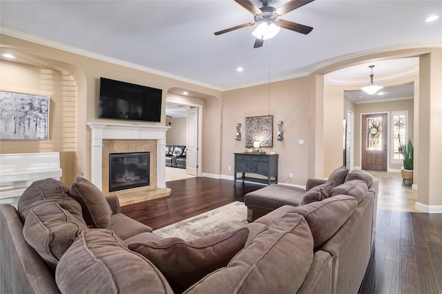 living room featuring ceiling fan, hardwood / wood-style floors, ornamental molding, and a tiled fireplace