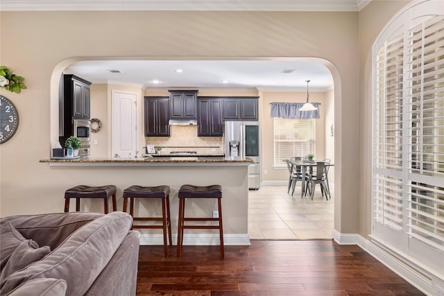 kitchen featuring kitchen peninsula, decorative backsplash, dark wood-type flooring, light stone countertops, and stainless steel appliances