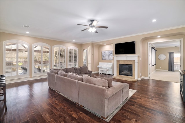 living room with ceiling fan, a fireplace, ornamental molding, and dark wood-type flooring