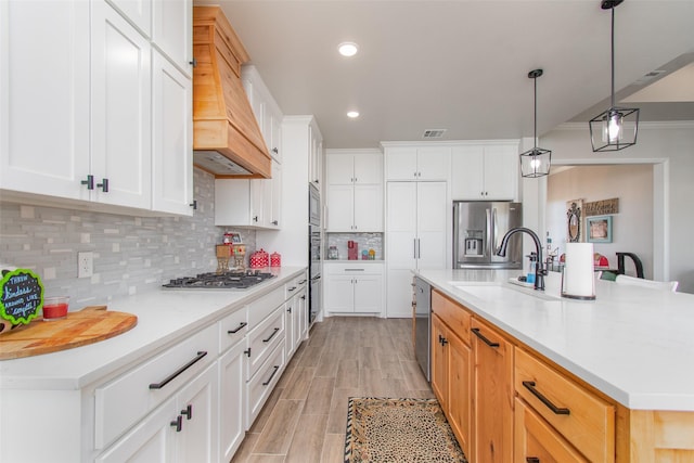 kitchen with a center island with sink, stainless steel appliances, backsplash, hanging light fixtures, and white cabinets