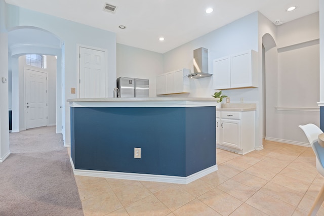 kitchen with white cabinetry, stainless steel fridge, wall chimney exhaust hood, and an island with sink