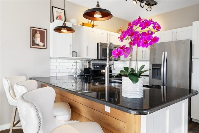 kitchen with decorative backsplash, white cabinetry, hanging light fixtures, appliances with stainless steel finishes, and dark hardwood / wood-style flooring