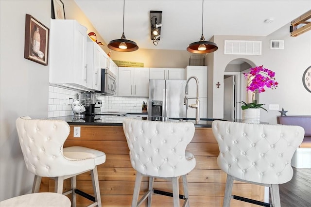 kitchen featuring white cabinetry, stainless steel appliances, backsplash, hanging light fixtures, and a breakfast bar