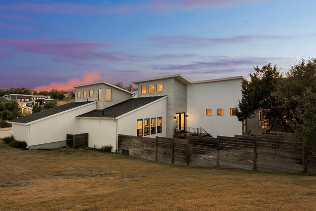 back house at dusk featuring a lawn