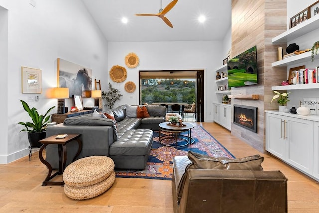 living room featuring ceiling fan, a tiled fireplace, light hardwood / wood-style flooring, and a towering ceiling