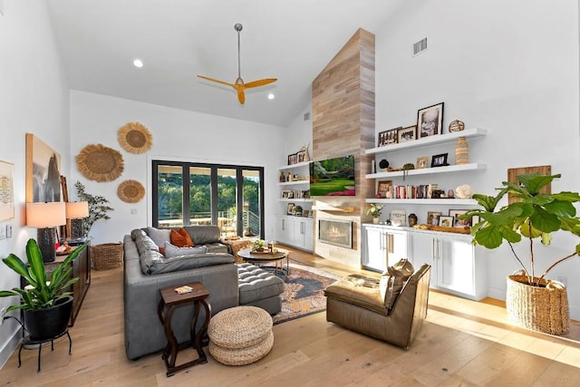 living room with a tiled fireplace, ceiling fan, high vaulted ceiling, and light wood-type flooring