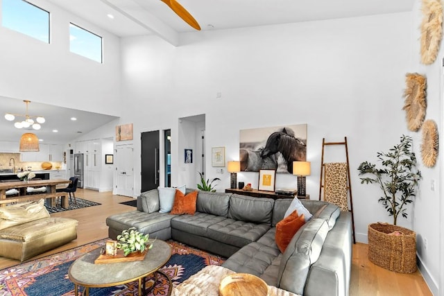 living room featuring beamed ceiling, a high ceiling, and light wood-type flooring