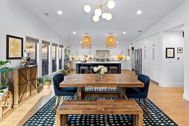 dining space with an inviting chandelier, sink, light hardwood / wood-style floors, and vaulted ceiling