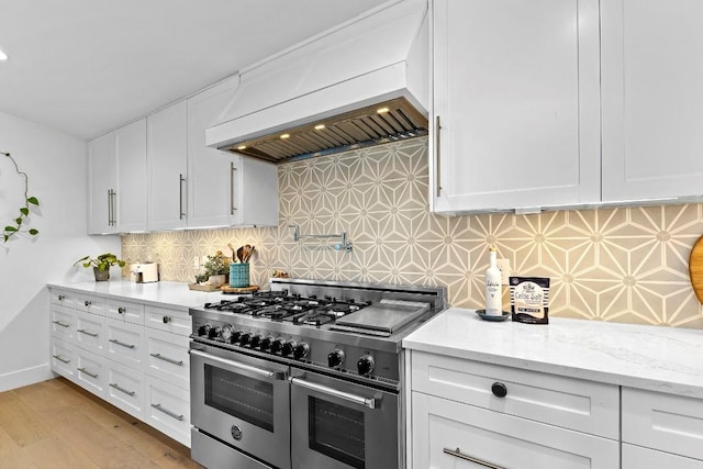 kitchen featuring light wood-type flooring, double oven range, custom range hood, decorative backsplash, and white cabinets