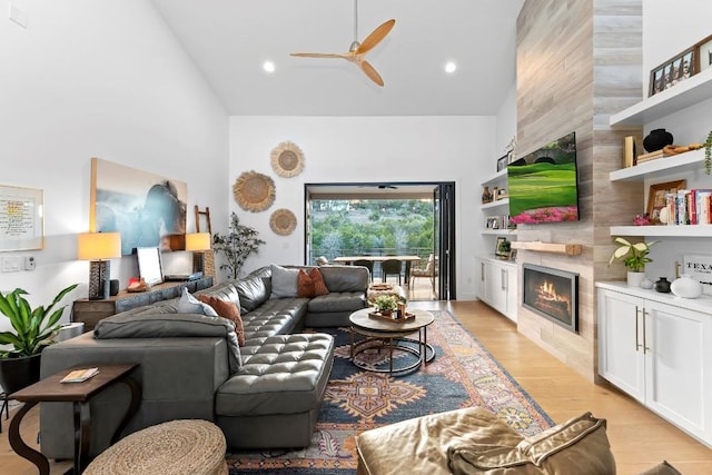 living room with high vaulted ceiling, a tile fireplace, ceiling fan, and light wood-type flooring