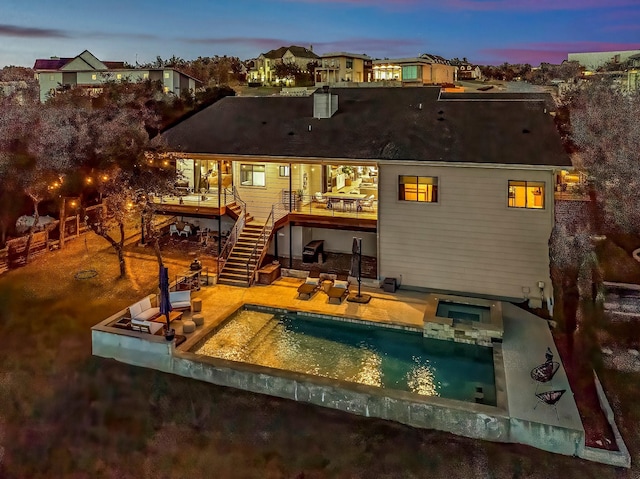 back house at dusk featuring a patio and a pool with hot tub