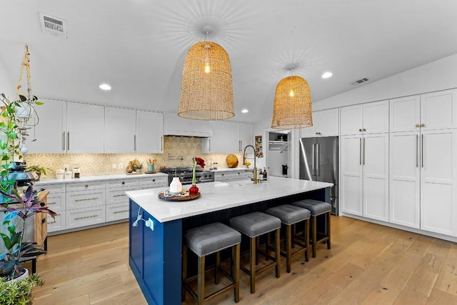 kitchen featuring pendant lighting, white cabinetry, backsplash, high end appliances, and a center island with sink