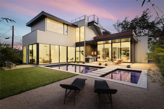 back house at dusk featuring a patio area, a yard, and a balcony