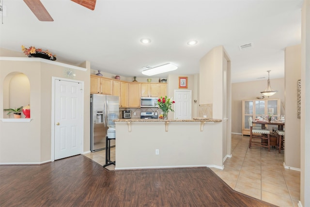 kitchen featuring a kitchen bar, kitchen peninsula, appliances with stainless steel finishes, light wood-type flooring, and light stone countertops