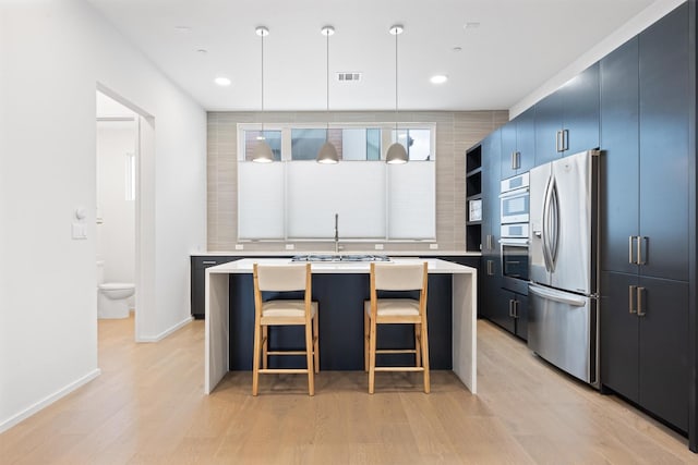 kitchen with light wood-type flooring, stainless steel appliances, hanging light fixtures, and a kitchen island