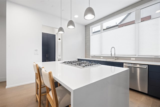 kitchen with appliances with stainless steel finishes, a center island, decorative light fixtures, light wood-type flooring, and sink