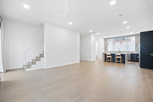 unfurnished living room featuring light hardwood / wood-style floors, sink, and ceiling fan