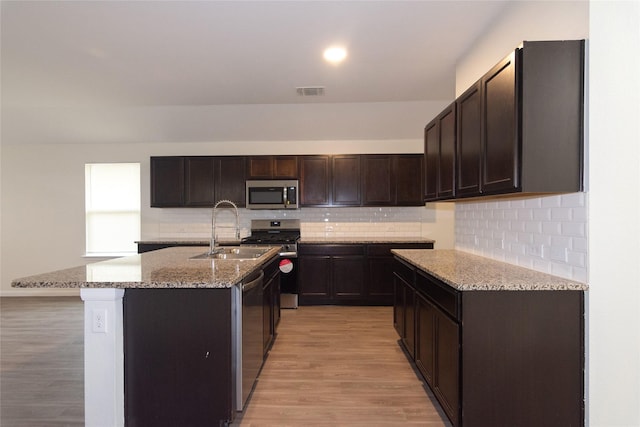 kitchen featuring appliances with stainless steel finishes, an island with sink, sink, light hardwood / wood-style flooring, and dark brown cabinets