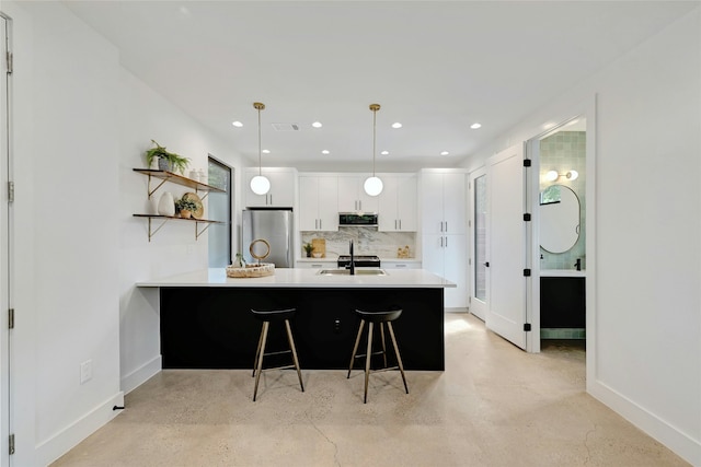 kitchen featuring sink, white cabinets, stainless steel fridge, a kitchen breakfast bar, and hanging light fixtures