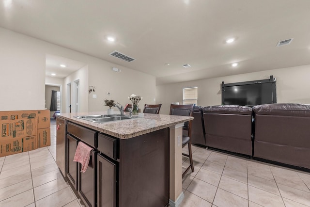 kitchen featuring sink, light tile patterned floors, stainless steel dishwasher, a center island with sink, and dark brown cabinets