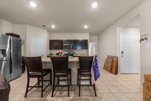 kitchen with light tile patterned floors, a breakfast bar area, stainless steel appliances, a kitchen island, and light stone counters