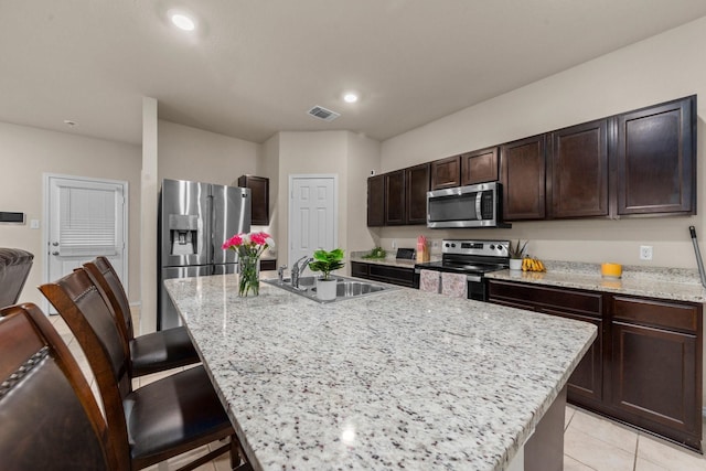 kitchen with a center island with sink, stainless steel appliances, light tile patterned flooring, light stone countertops, and sink