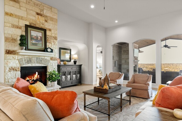 living room with ceiling fan, a stone fireplace, and light hardwood / wood-style floors